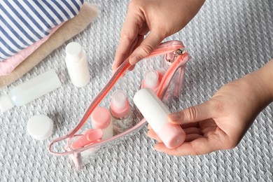 Photo of Woman putting small bottle with personal care product into plastic bag, closeup. Cosmetic travel kit