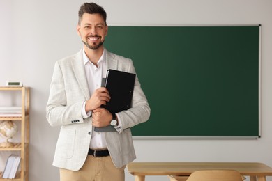 Photo of Happy teacher with stationery in classroom. Space for text