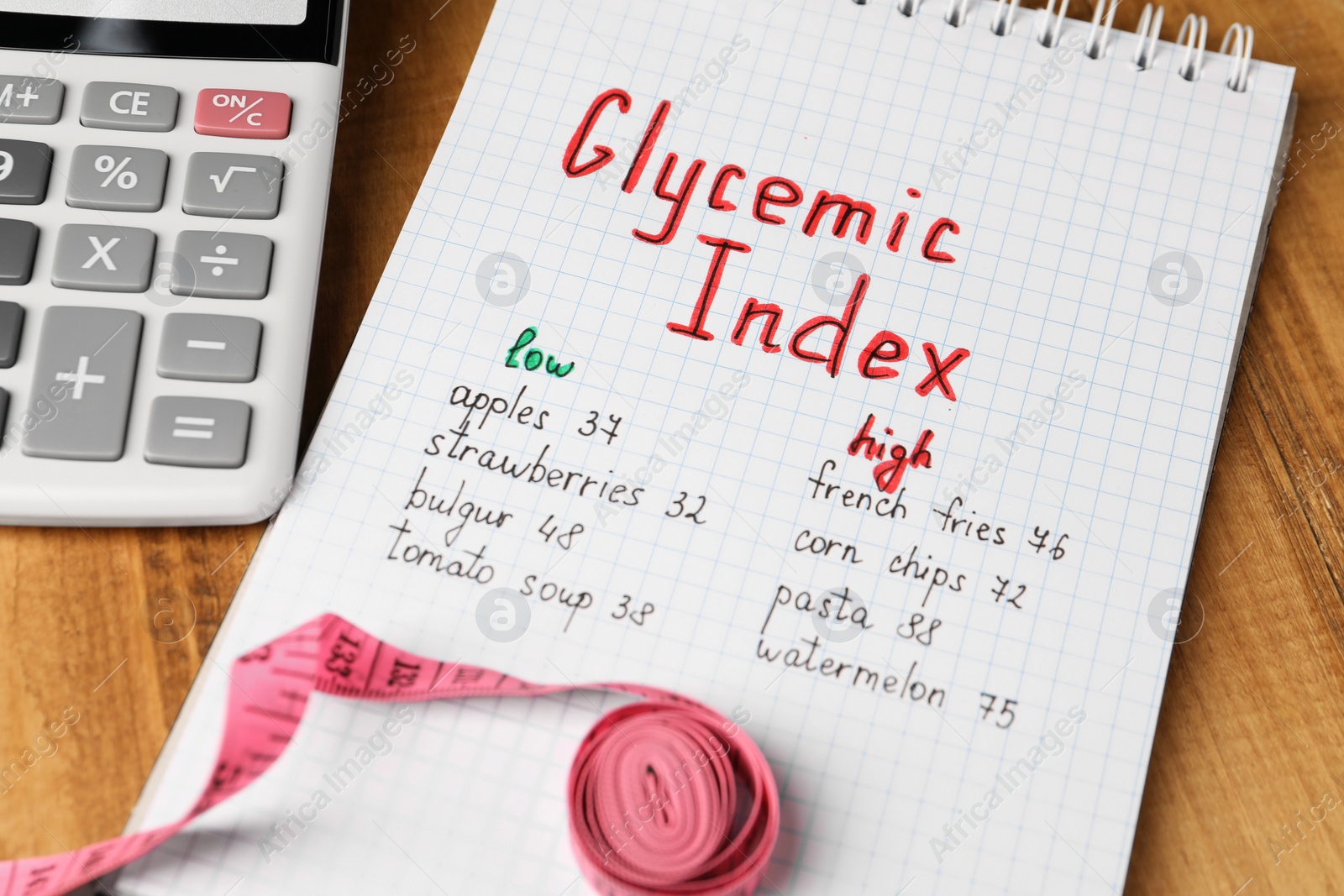 Photo of List with products of low and high glycemic index in notebook calculator and measuring tape on wooden table, closeup