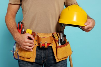 Photo of Professional builder with hard hat and tool belt on light blue background, closeup