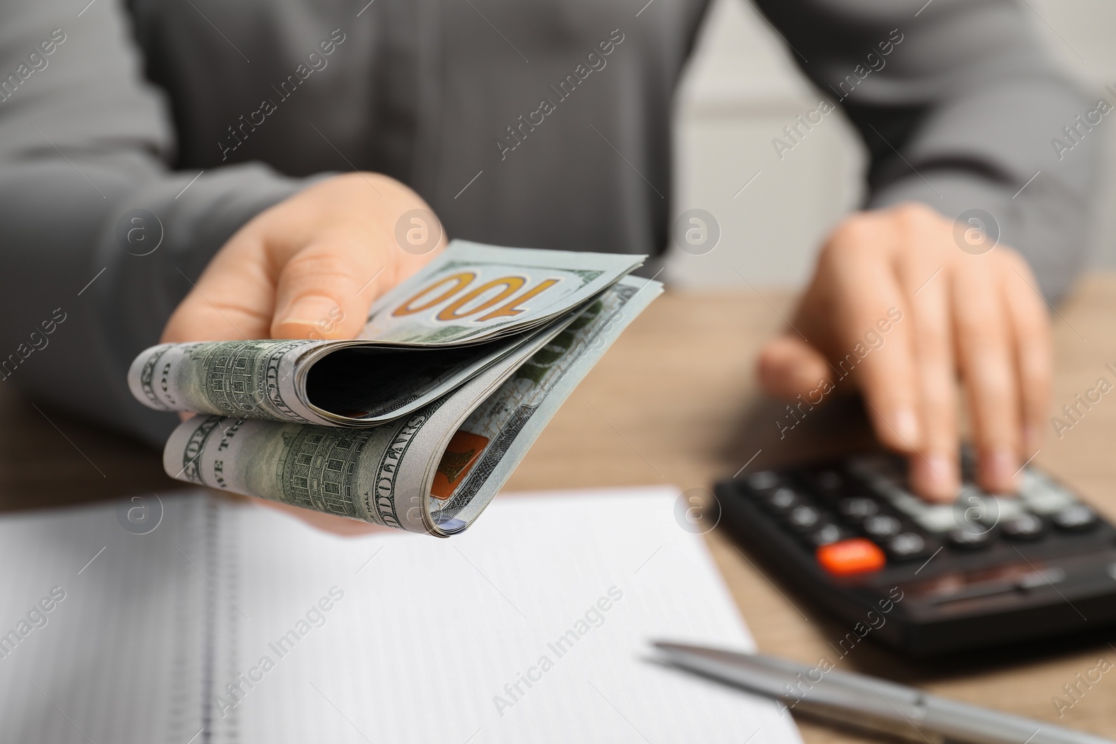 Photo of Money exchange. Woman holding dollar banknotes at wooden table, closeup