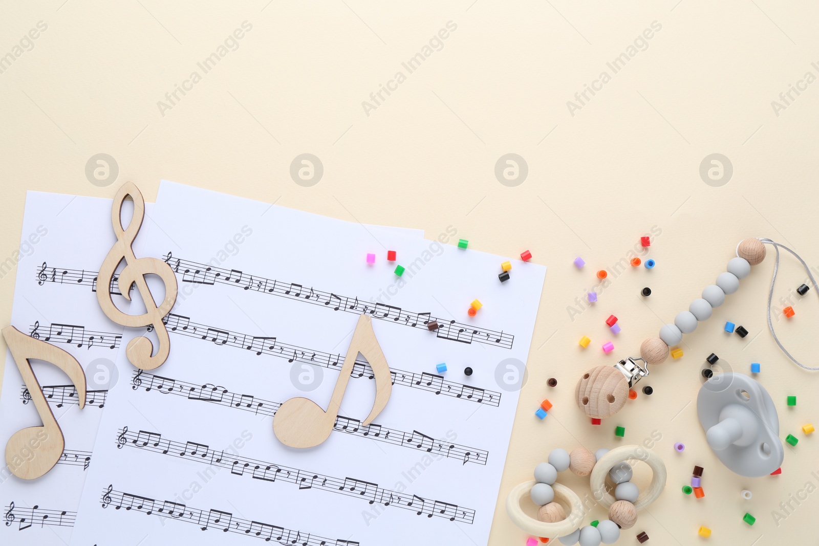 Photo of Wooden notes, music sheets and toys on beige background, flat lay with space for text. Baby song concept