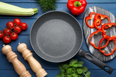 Photo of Empty frying pan, fresh vegetables and herbs on blue wooden table, flat lay