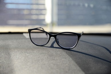 Photo of New stylish glasses on dashboard in car