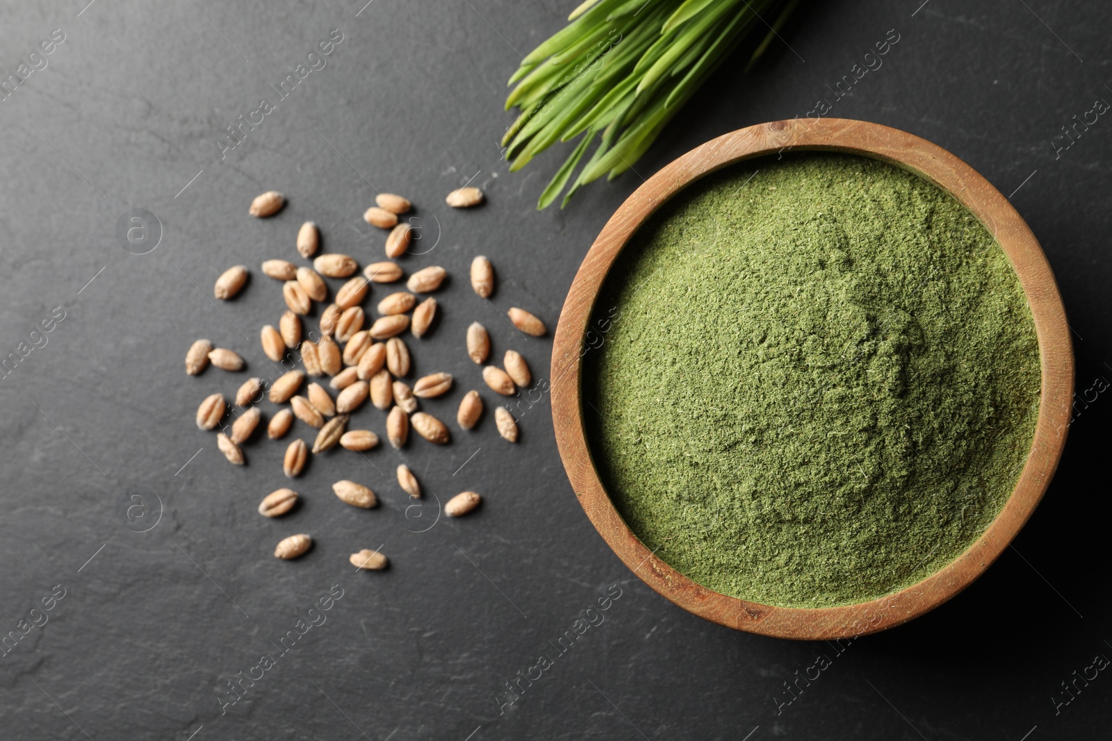 Photo of Wheat grass powder in bowl, seeds and fresh sprouts on grey textured table, flat lay