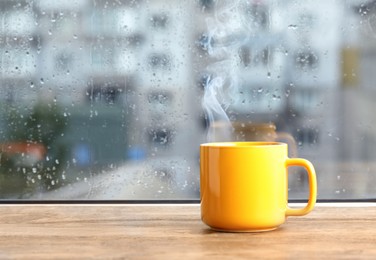 Photo of Cup of hot drink near window on rainy day. Space for text