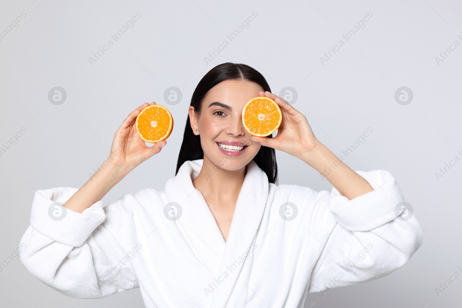 Photo of Woman in bathrobe holding juicy cut orange on light grey background. Spa treatment