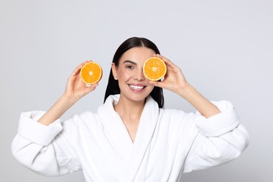 Woman in bathrobe holding juicy cut orange on light grey background. Spa treatment