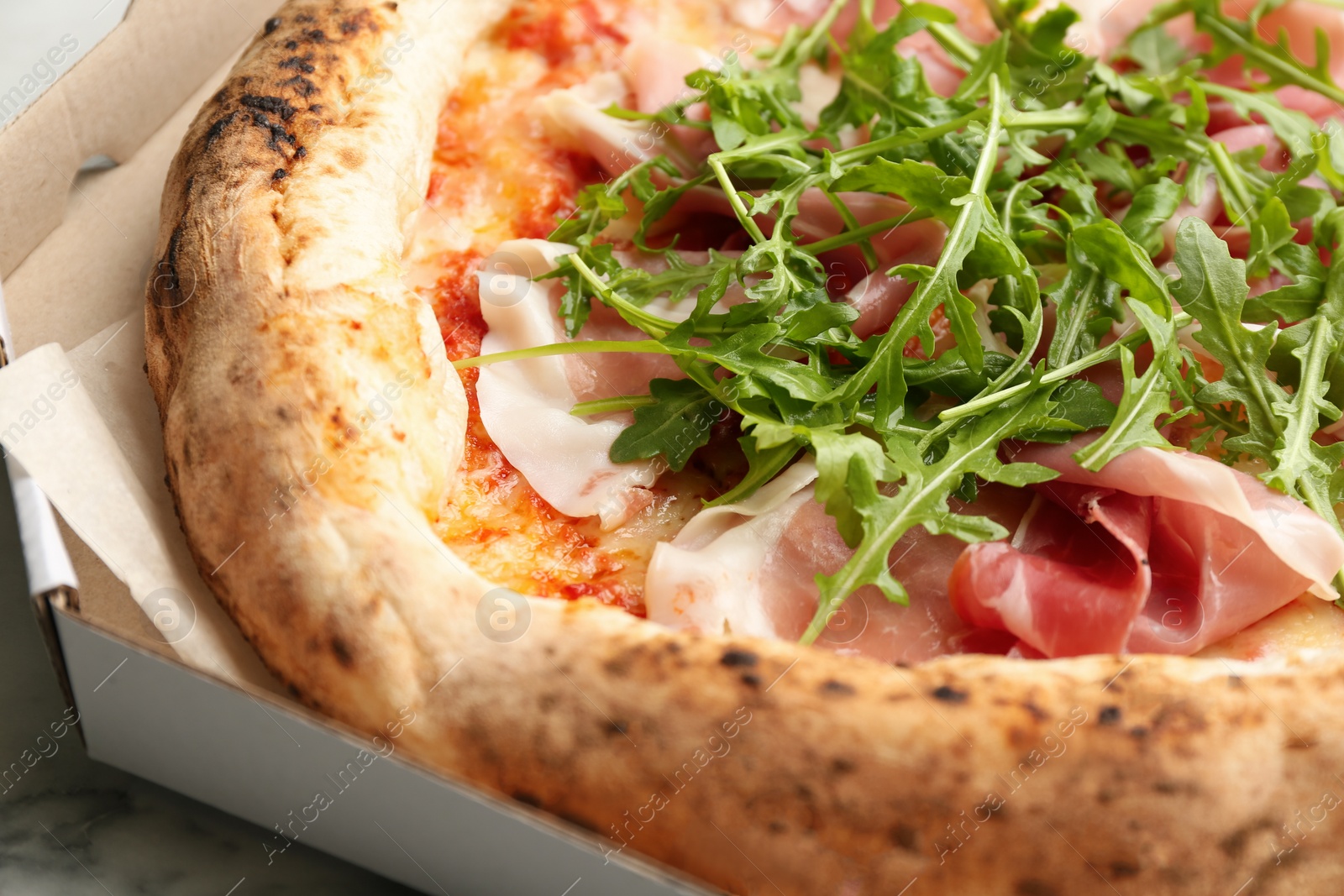 Photo of Tasty pizza with meat and arugula in cardboard box, closeup