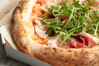 Photo of Tasty pizza with meat and arugula in cardboard box, closeup