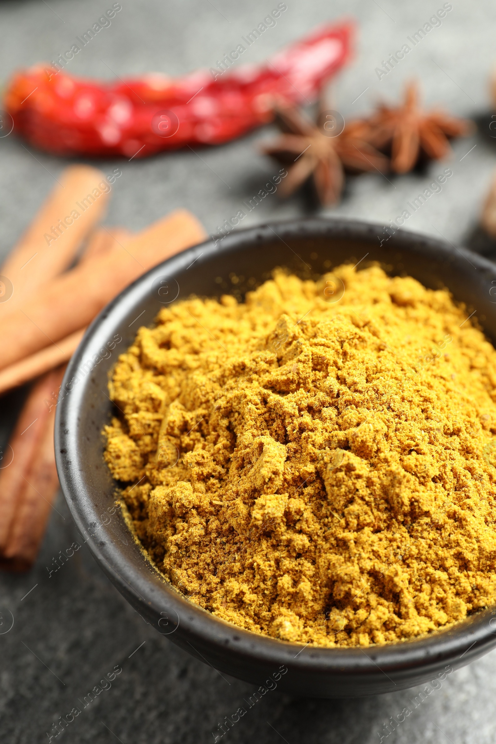 Photo of Dry curry powder in bowl on dark textured table, closeup