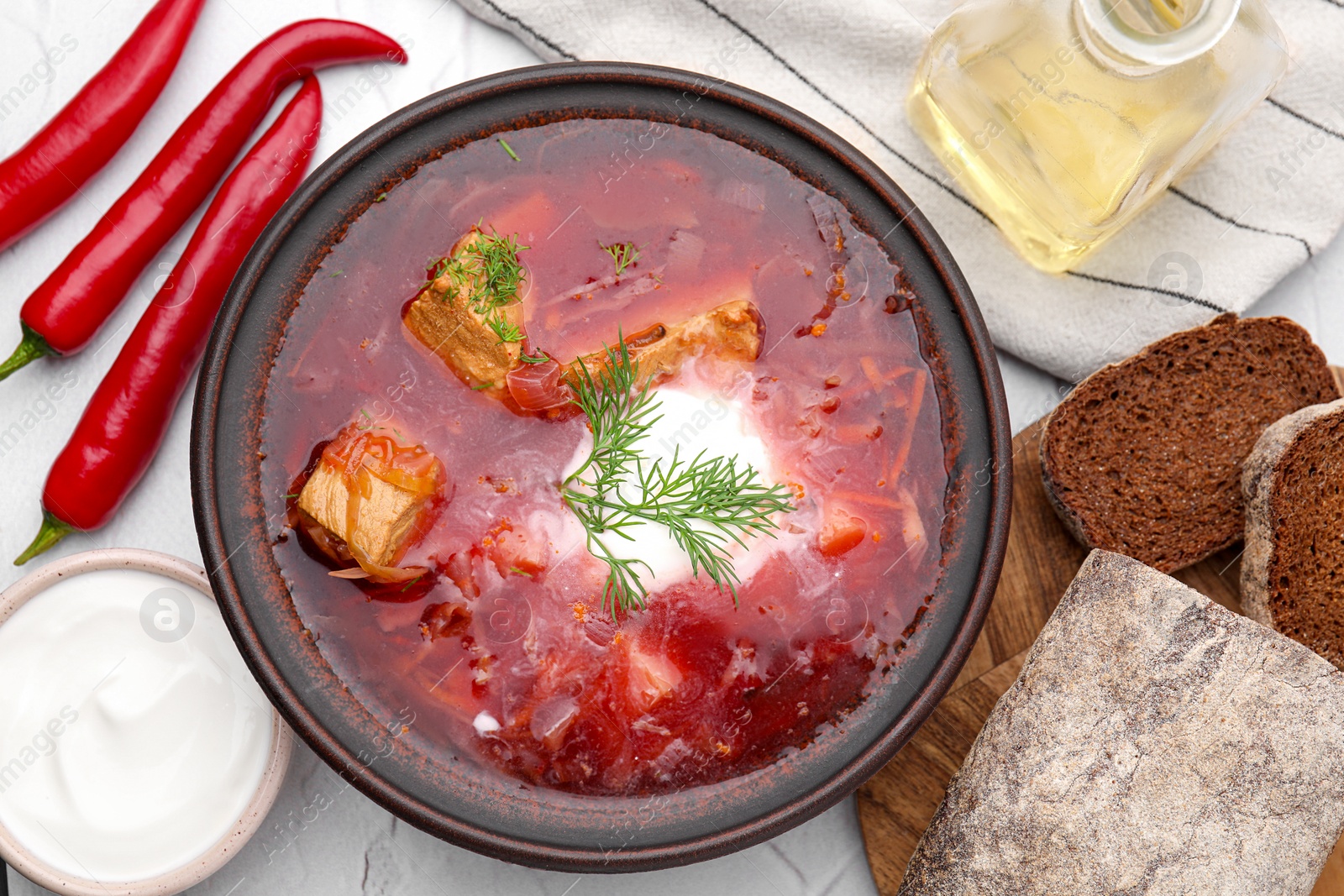 Photo of Tasty borscht with sour cream in bowl served on white table, flat lay