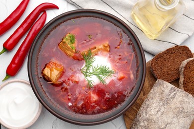 Photo of Tasty borscht with sour cream in bowl served on white table, flat lay