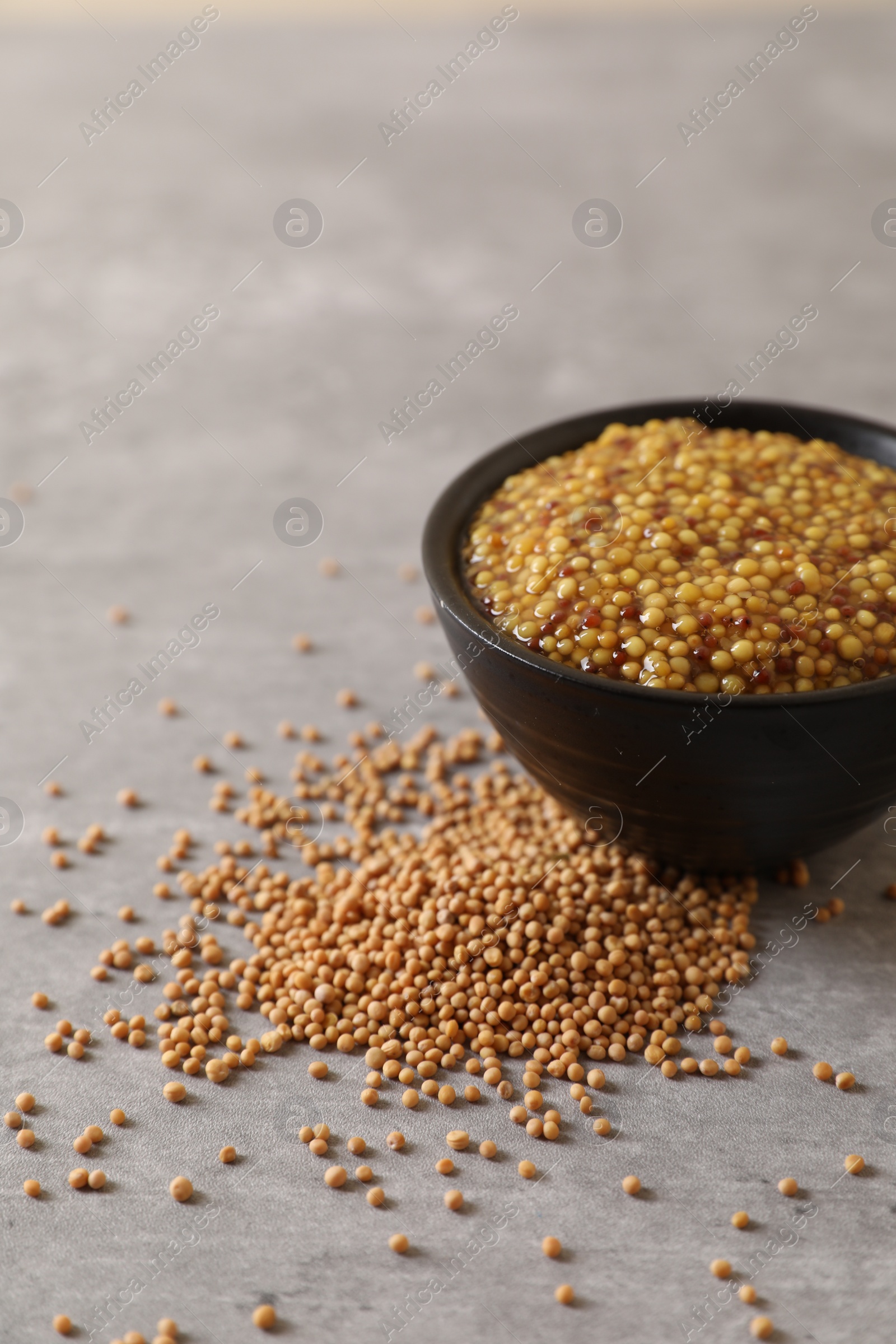Photo of Bowl of whole grain mustard and seeds on grey table, closeup