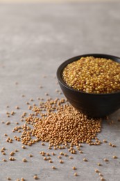 Photo of Bowl of whole grain mustard and seeds on grey table, closeup