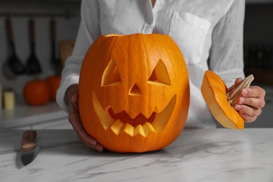 Photo of Woman with carved pumpkin for Halloween at white marble table in kitchen, closeup
