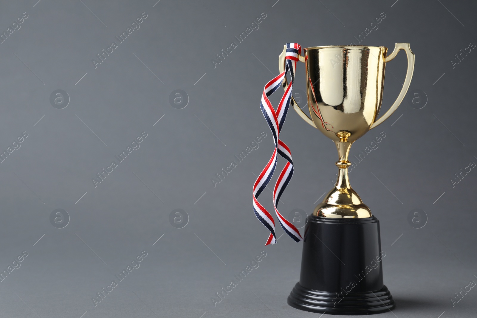 Photo of Golden trophy cup with ribbon on grey background. Space for text