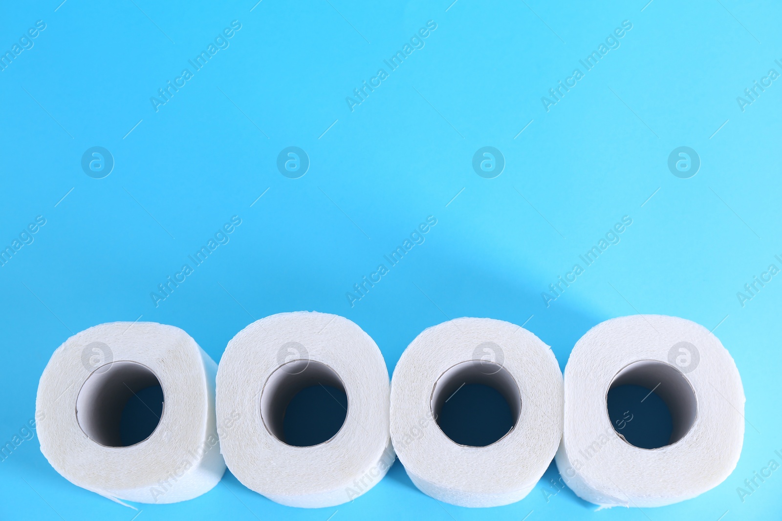 Photo of Soft toilet paper rolls on light blue background, flat lay. Space for text