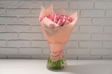 Bouquet of beautiful pink tulips in vase on white table near brick wall