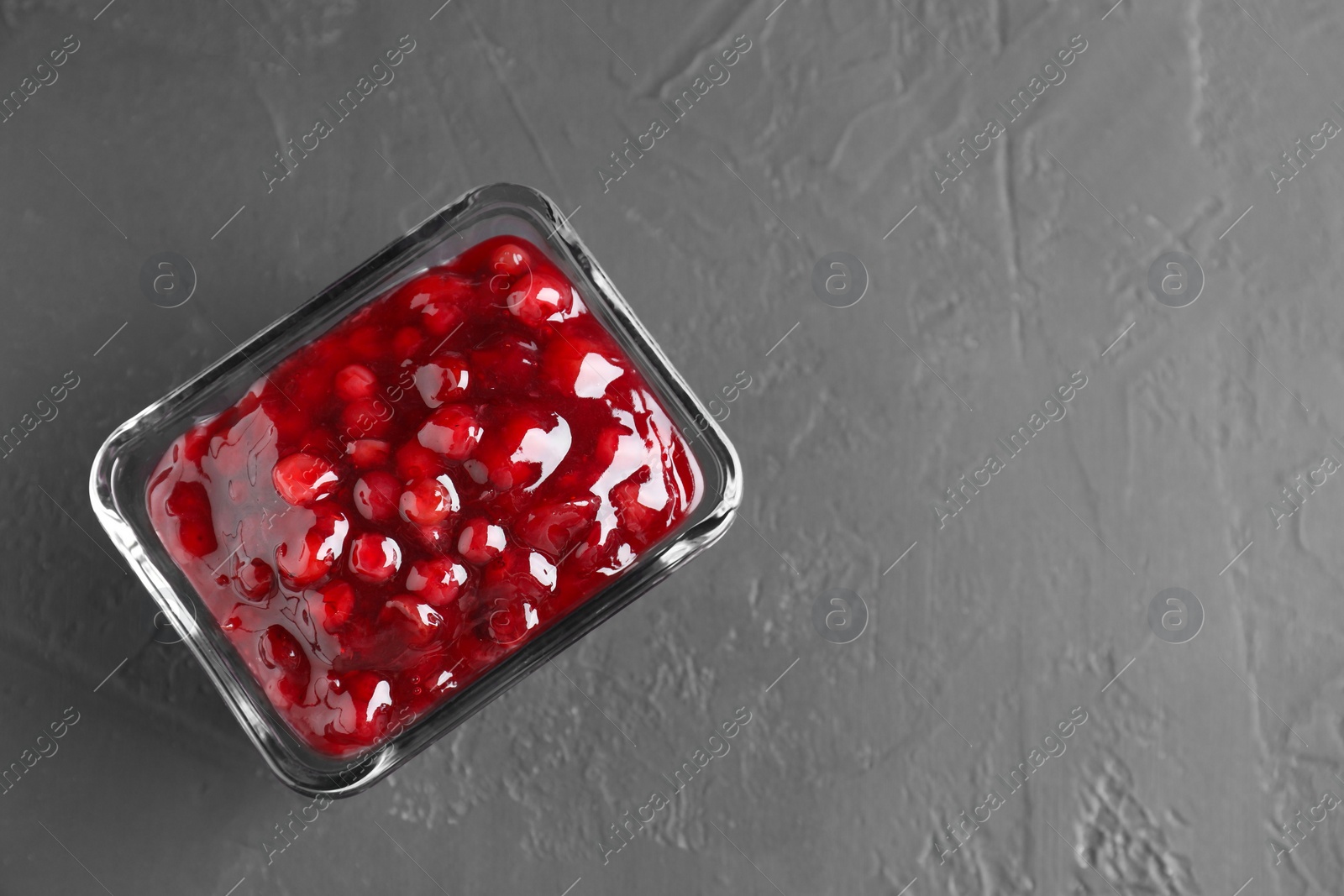 Photo of Fresh cranberry sauce in glass bowl on gray textured table, top view. Space for text