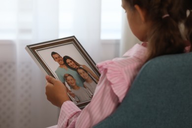 Photo of Little girl holding framed family photo indoors, closeup