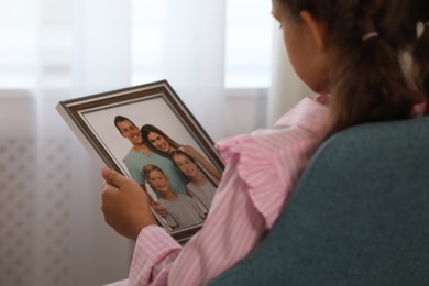 Little girl holding framed family photo indoors, closeup