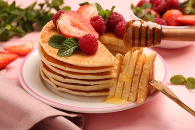 Dripping honey onto delicious pancakes with fresh berries on pink table, closeup