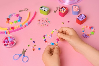 Photo of Child making beaded jewelry and different supplies on pink background, above view. Handmade accessories
