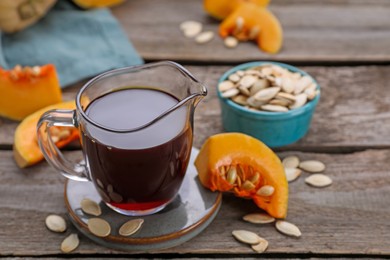 Photo of Fresh pumpkin seed oil in glass pitcher on wooden table. Space for text