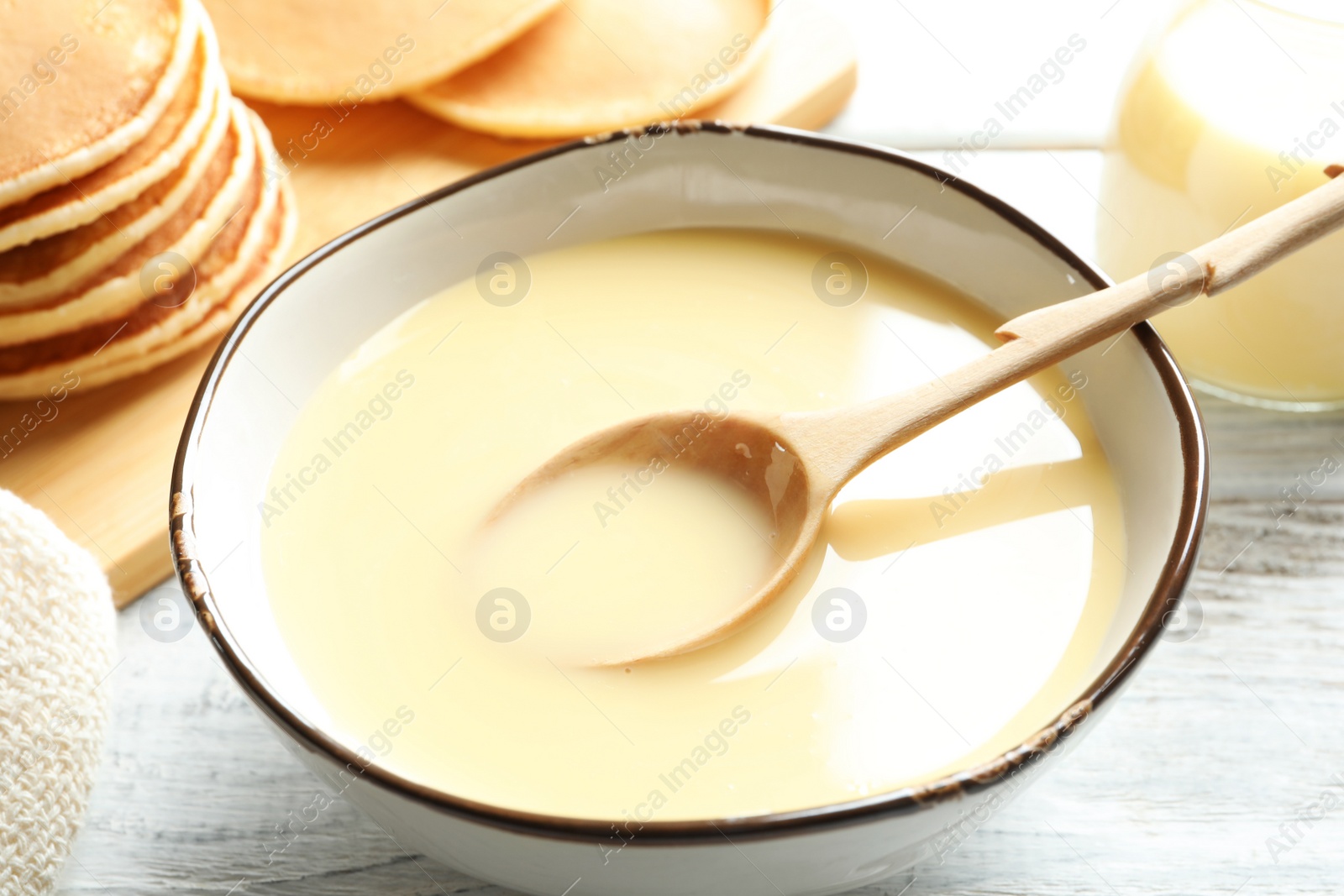 Photo of Bowl with condensed milk and spoon on table. Dairy products