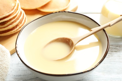 Photo of Bowl with condensed milk and spoon on table. Dairy products