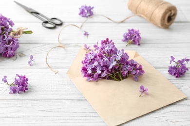 Photo of Envelope and beautiful blossoming lilac on table. Spring flowers
