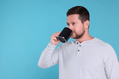 Man drinking from black mug on light blue background. Space for text