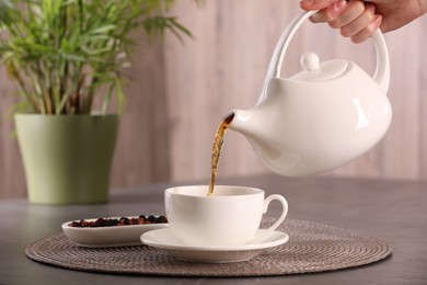 Photo of Woman pouring tea into cup at grey table, closeup