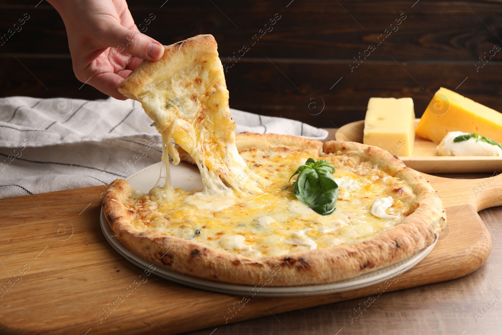 Photo of Woman taking piece of delicious cheese pizza at wooden table, closeup