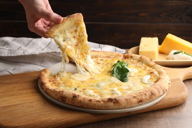 Photo of Woman taking piece of delicious cheese pizza at wooden table, closeup