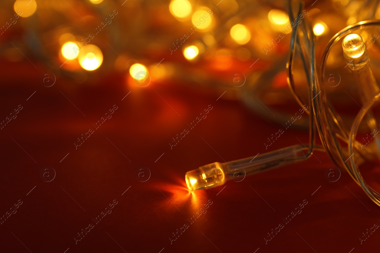 Photo of Glowing Christmas lights on red background, closeup