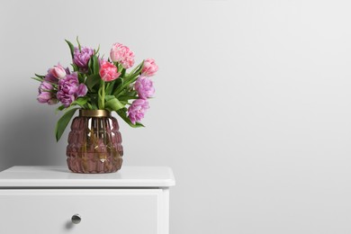 Photo of Beautiful bouquet of colorful tulip flowers on white bedside table near white wall, space for text