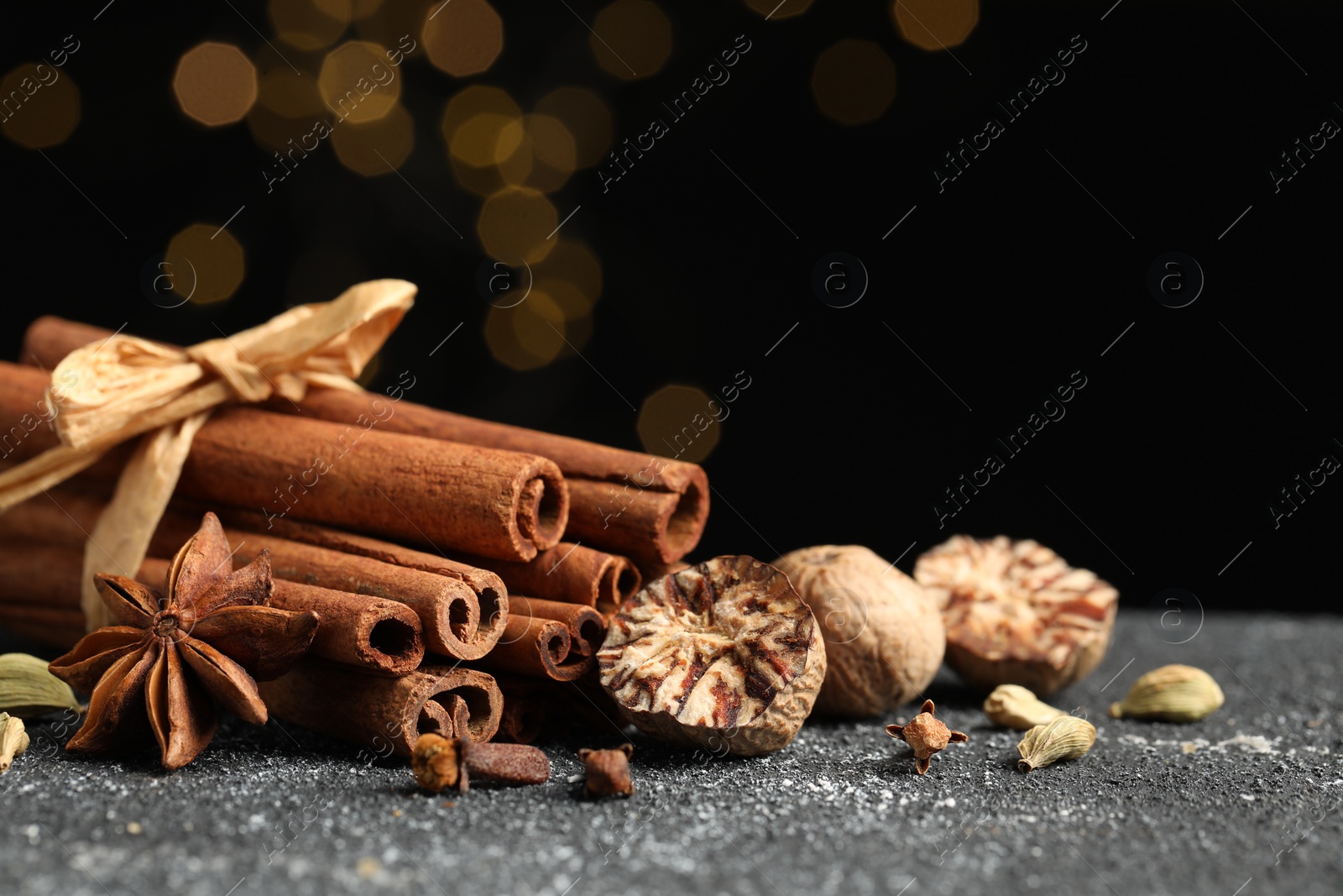 Photo of Different aromatic spices on grey textured table against black background, closeup. Space for text