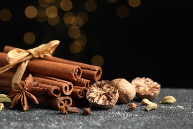 Different aromatic spices on grey textured table against black background, closeup. Space for text