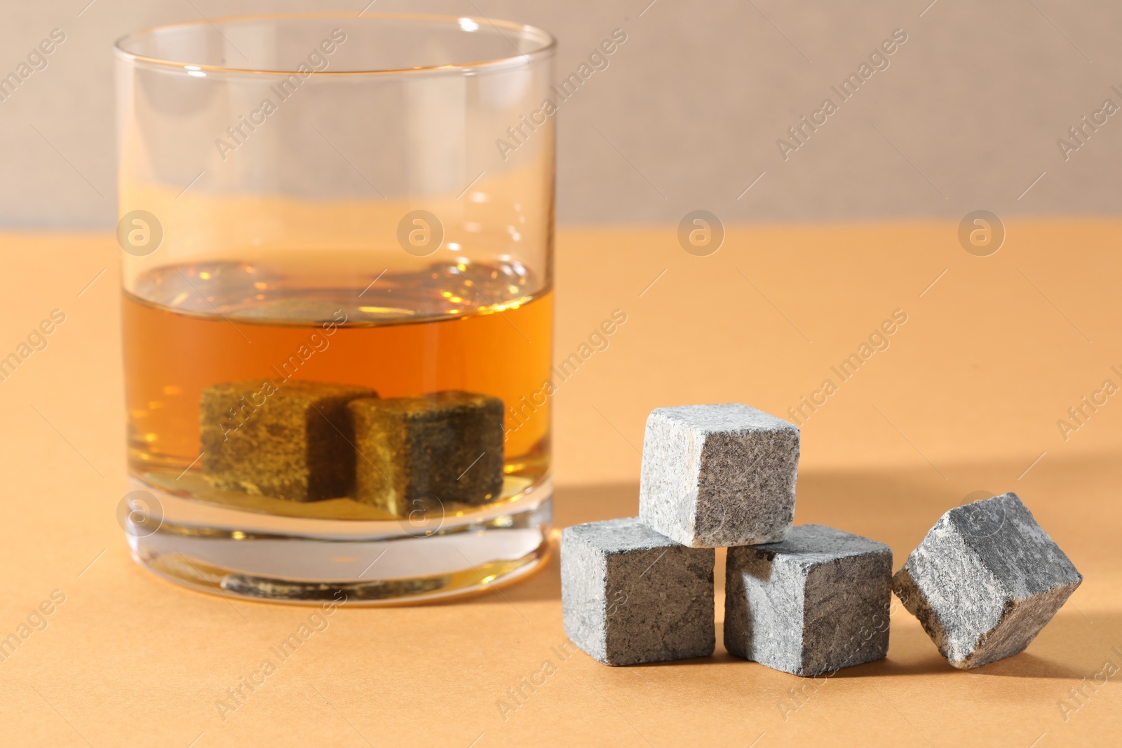 Photo of Whiskey stones and drink in glass on orange table, closeup