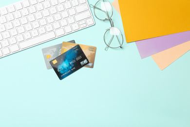 Photo of Credit cards, computer keyboard and glasses on light blue background, flat lay. Space for text