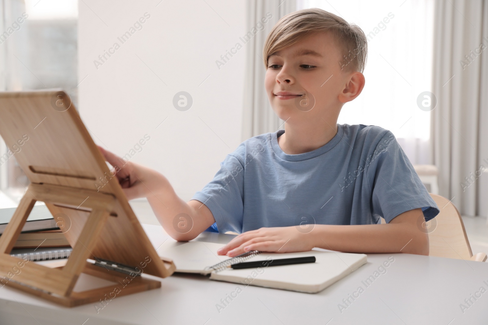 Photo of Boy doing homework with tablet at table indoors