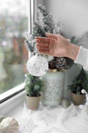 Woman holding Christmas bauble near window indoors, closeup