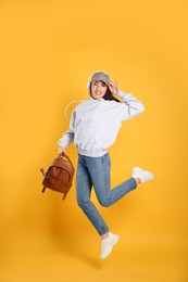 Photo of Beautiful young woman with stylish leather backpack and headphones jumping on yellow background