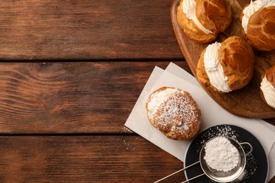 Delicious profiteroles with cream filling and powdered sugar on wooden table, flat lay. Space for text