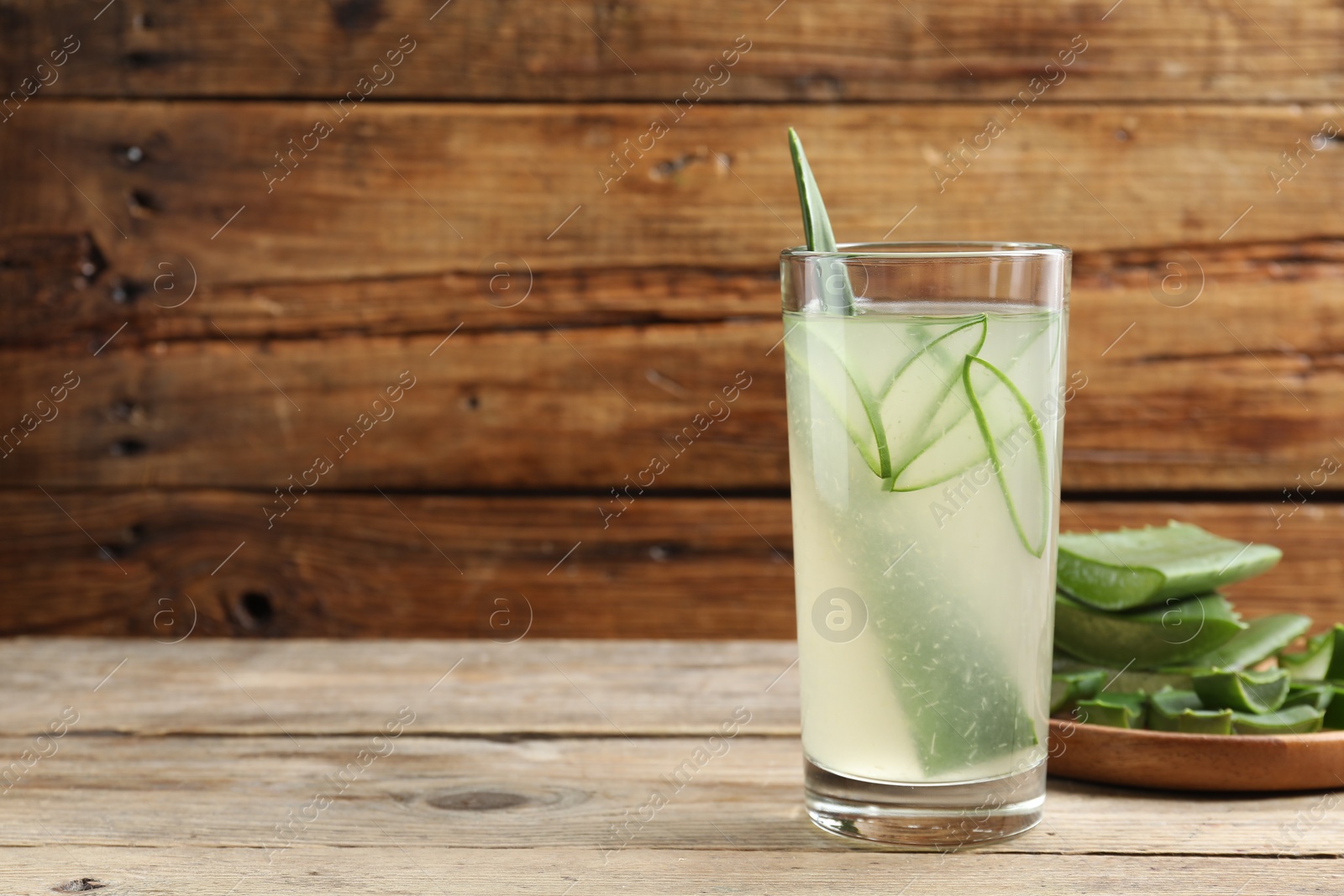 Photo of Tasty aloe juice in glass and cut fresh leaves on wooden table, space for text