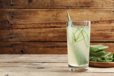 Photo of Tasty aloe juice in glass and cut fresh leaves on wooden table, space for text