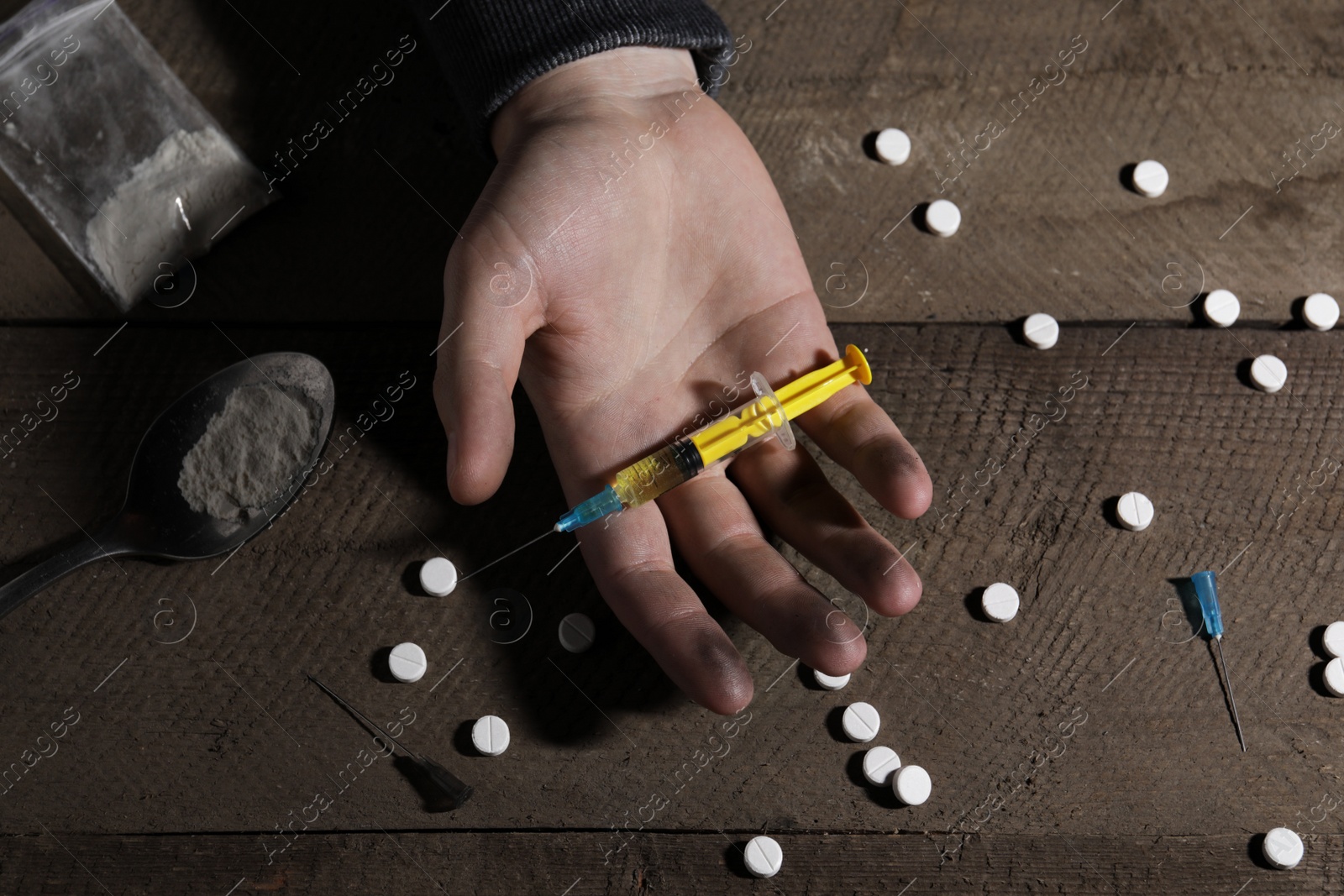 Photo of Addicted man with syringe near drugs at wooden table, top view