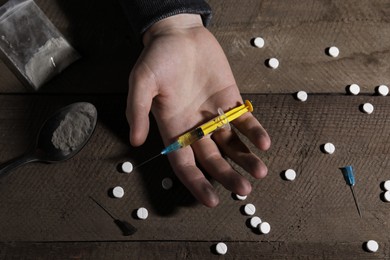 Photo of Addicted man with syringe near drugs at wooden table, top view